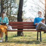 Woman and man in social distancing sitting on bench in park