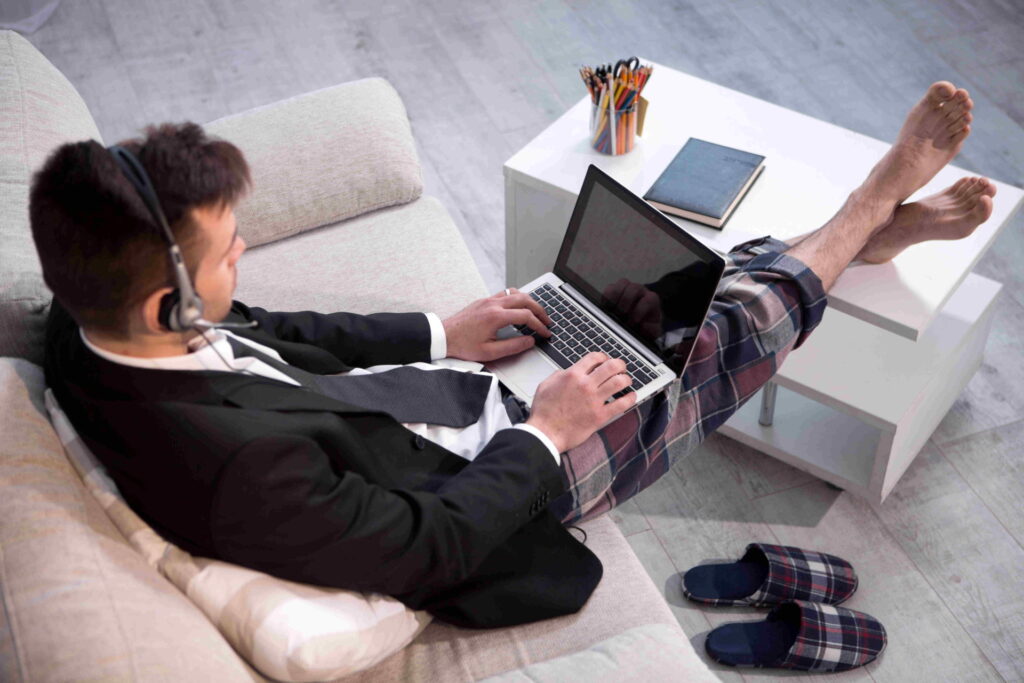 Man typing on laptop working on freelance at home. Up view on a man in casual trousers and jacket keyboarding on computer.