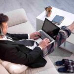 Man typing on laptop working on freelance at home. Up view on a man in casual trousers and jacket keyboarding on computer.